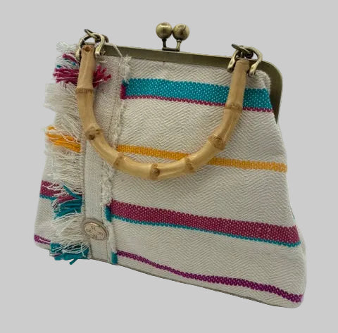 A woven handbag with a cream base, colorful horizontal stripes in teal, yellow, magenta, and purple, fringed tassels, and natural bamboo handles on a white studio background.