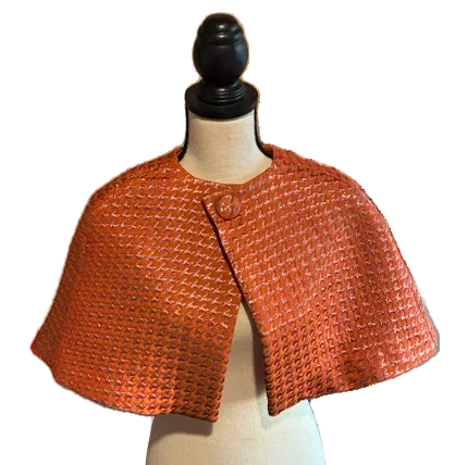 A cropped orange houndstooth  textured jacket with wide short sleeves, displayed on a cream dress form mannequin against a white background.
