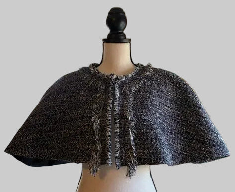 A navy and white  textured tweed cape jacket with fringed trim, displayed on a cream-colored dress form mannequin