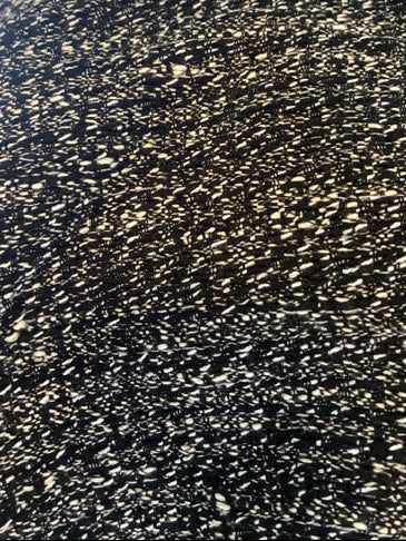 Close-up of navy tweed fabric with dense white and beige flecks, showing a self made fringe trim along the neckline.