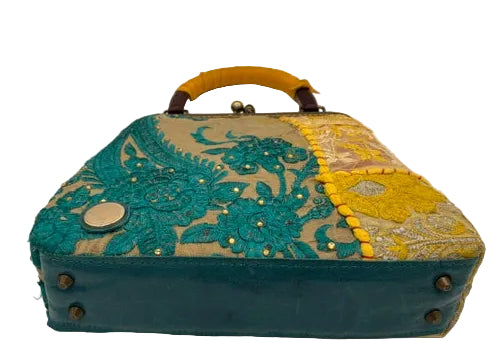A vintage-style handbag with a teal leather base, teal floral lace overlay, yellow fabric panels, and a mustard-yellow handle, photographed on a white surface.